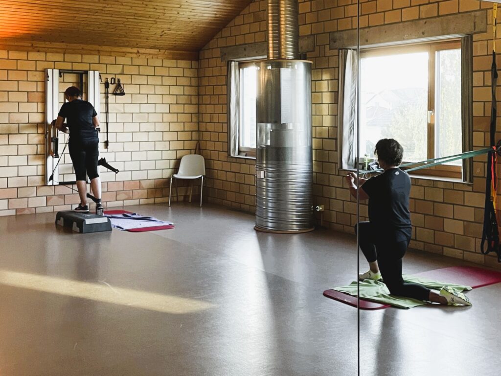 Kundinnen trainieren im Atrium Gym in Wigoltingen im Powerup-Kurs Kraft und Definition - Kundin links macht Glute-kicks am Eisenhorn-Kabelzug, Kundin rechts macht Pallow-Press mit Widerstandsband. 