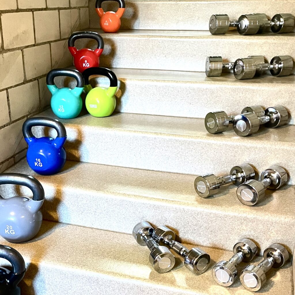 Bunte Kettlebells und silberne Kurzhanteln auf einer Treppe.